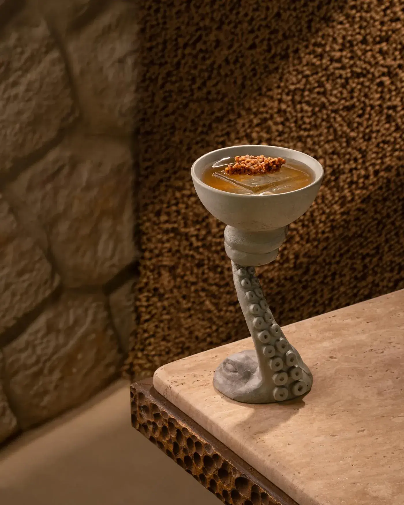 Concrete coupe on a cast tentacle stem, travertine finish, holding a cocktail
